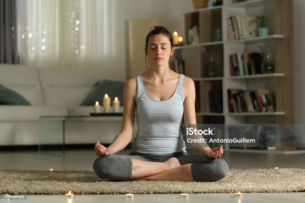 Front view full body portrait of a relaxed woman doing yoga exercise in the night at home with candles
